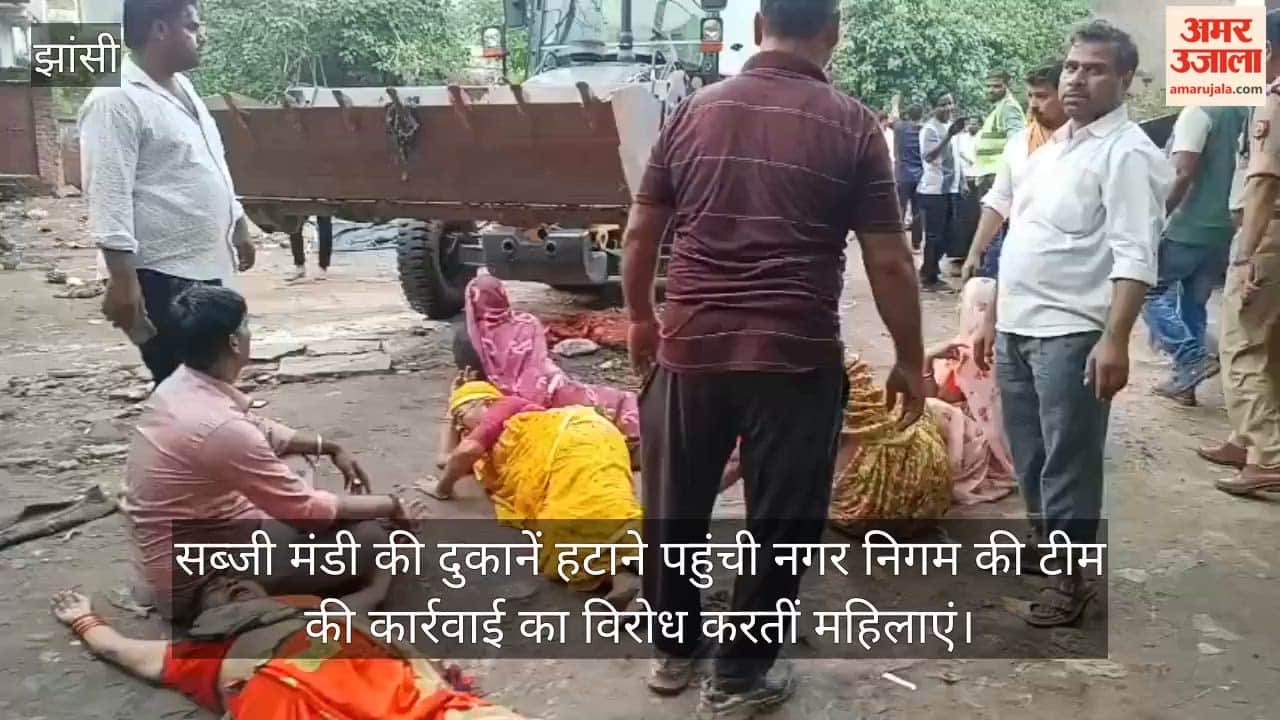 Team arrives to remove vegetable market shops; women lie down in front of JCB.
